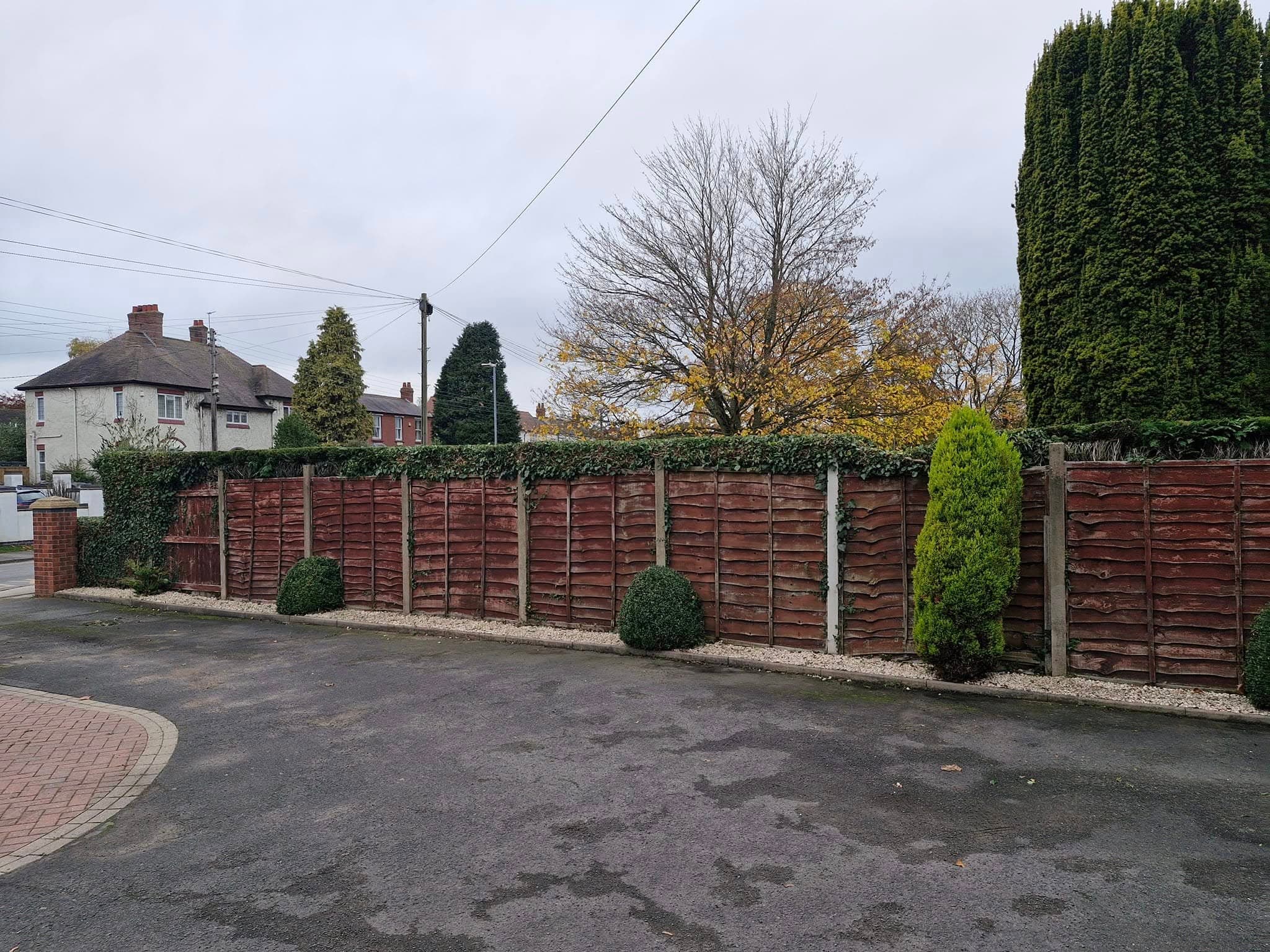A run of timber fence panels and hedging along a block-paved driveway