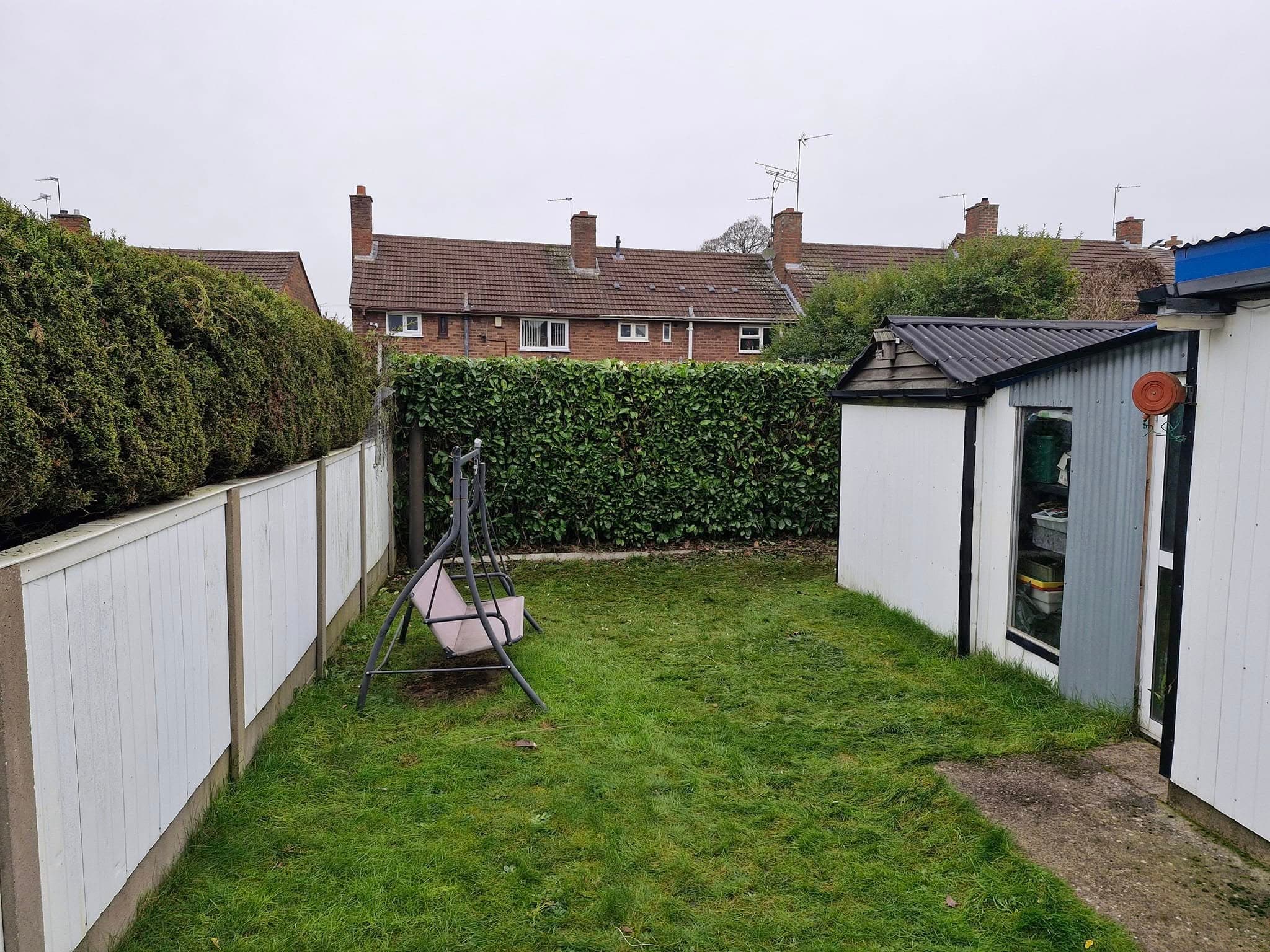 A boundary hedge trimmed level above fence panels at the back of a garden