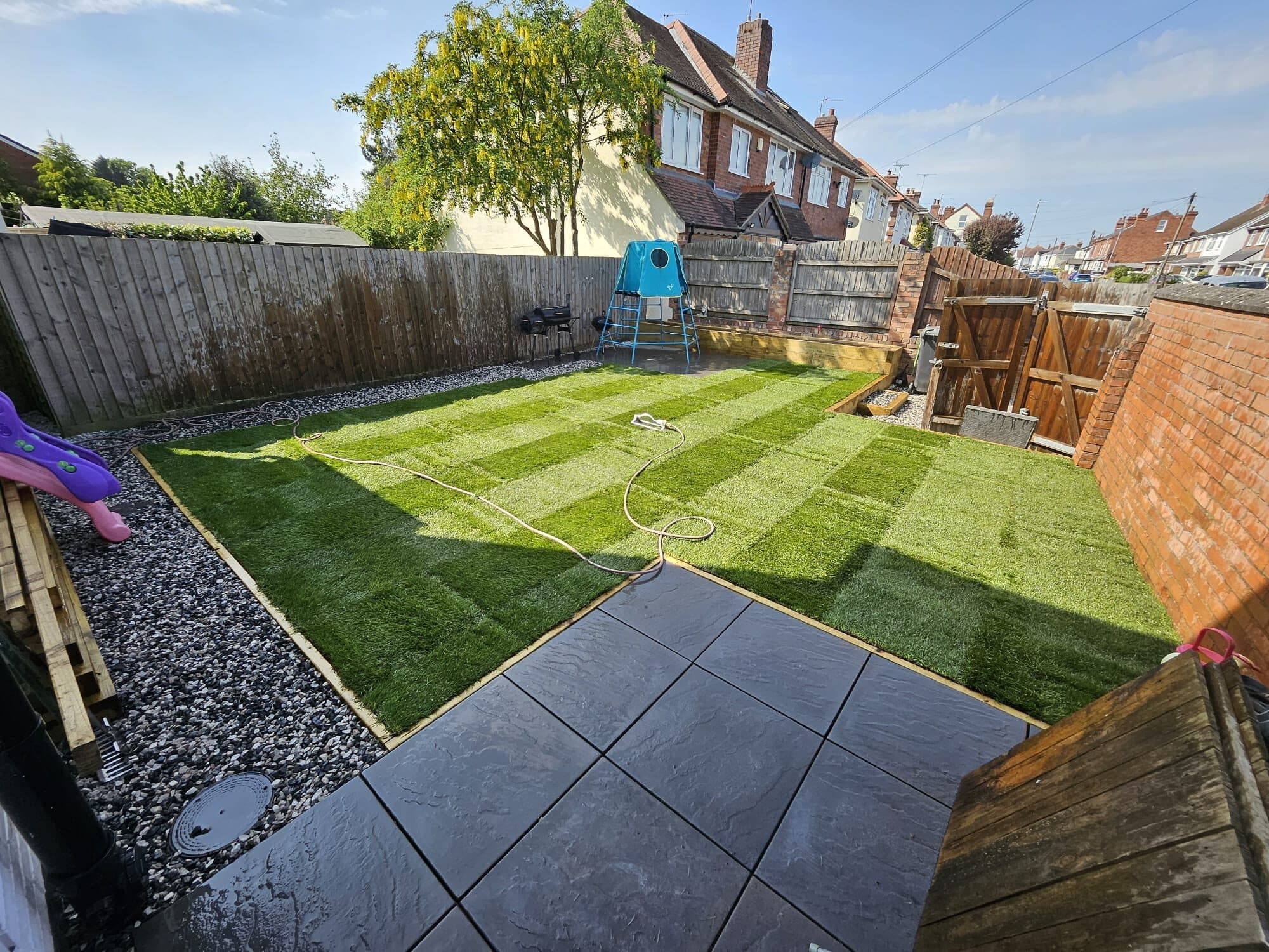 A back garden enclosed by timber fencing, with a freshly striped lawn and play equipment