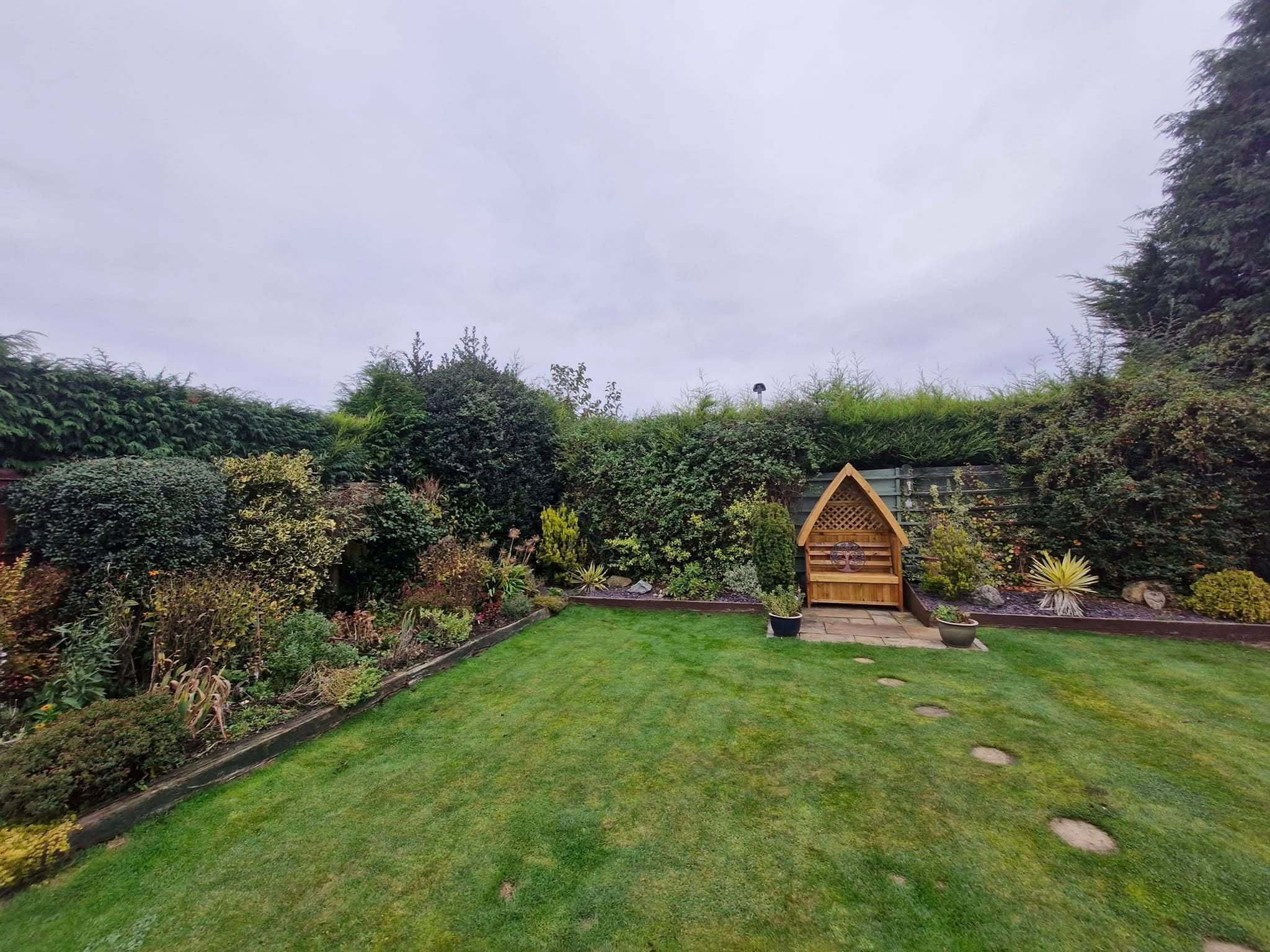 A kept lawn with planted borders and a hedge along the back boundary